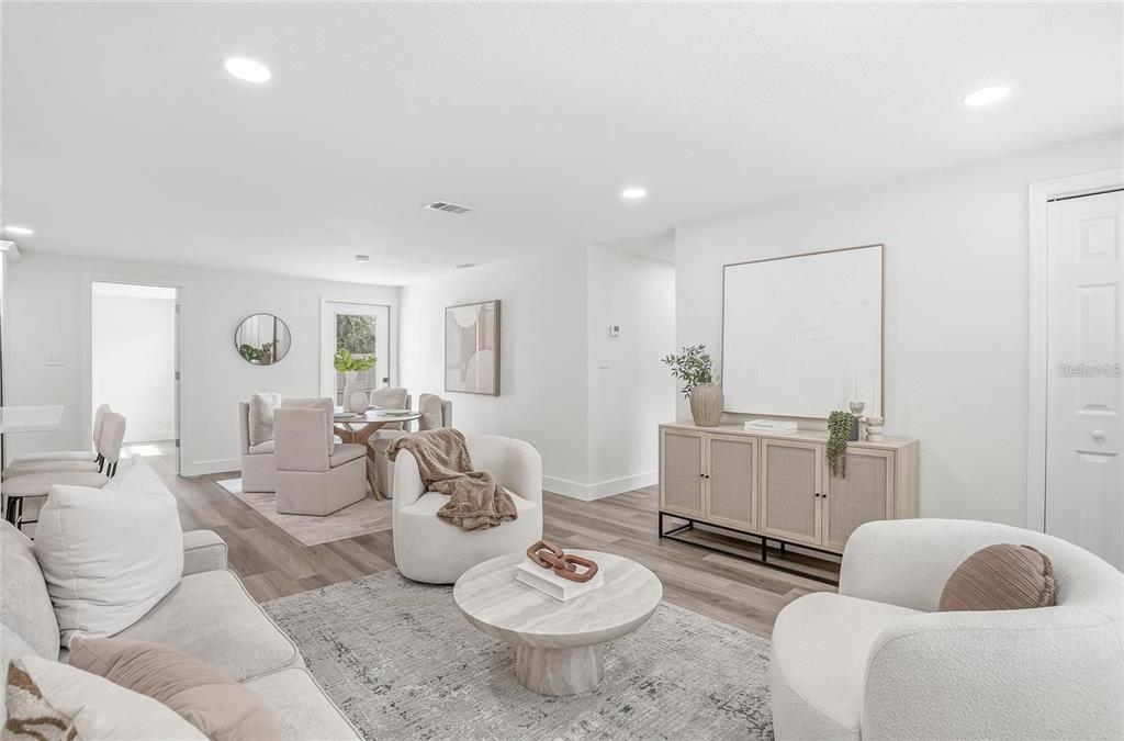A bright living and dining area with white walls, light wood floors, and modern furniture — 1004 IDLEBRIAR WAY, TARPON SPRINGS, FL