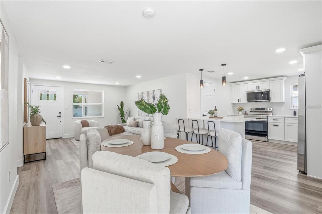 An open-concept living and dining area features light wood flooring, white cabinetry, and modern furniture — 1004 IDLEBRIAR WAY, TARPON SPRINGS, FL