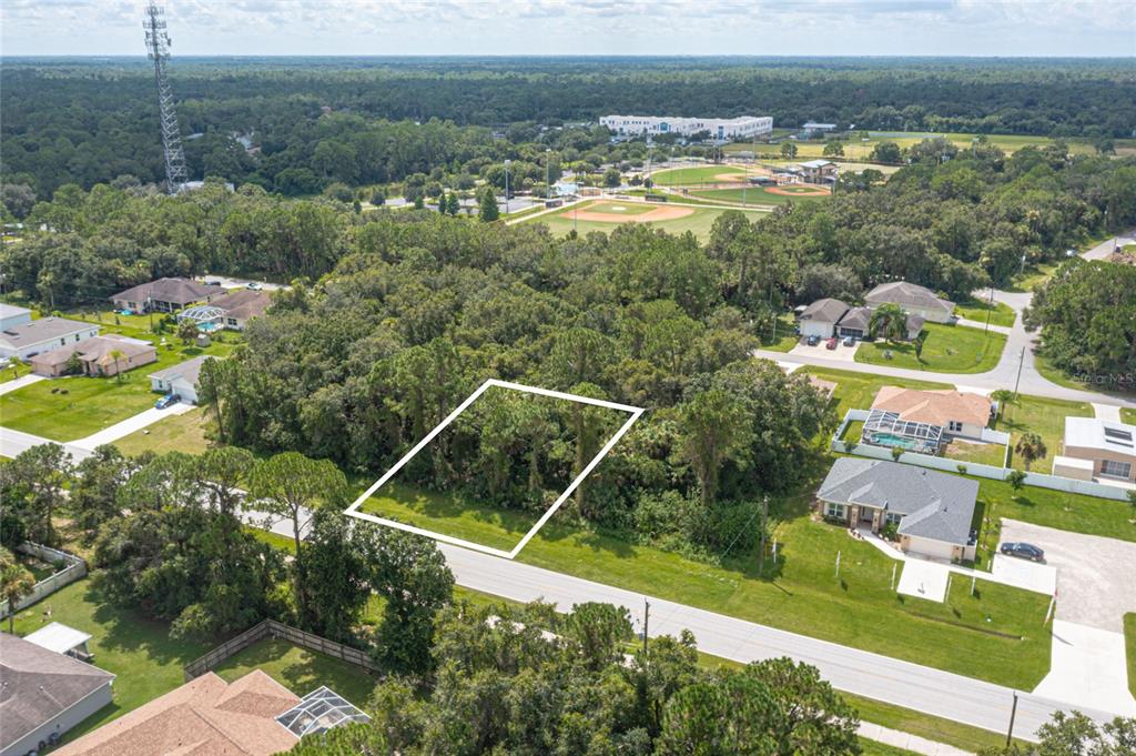 An aerial view shows a vacant, wooded residential lot outlined in white along a paved road — E PRICE BOULEVARD LOT 9, NORTH PORT, FL