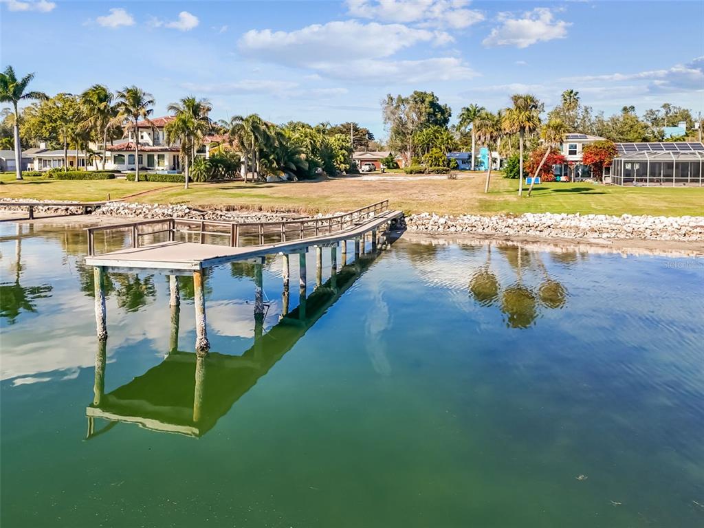 A long wooden pier extends into calm water in front of a grassy waterfront property — 6330 BAHAMA SHORES DRIVE S, ST PETERSBURG, FL
