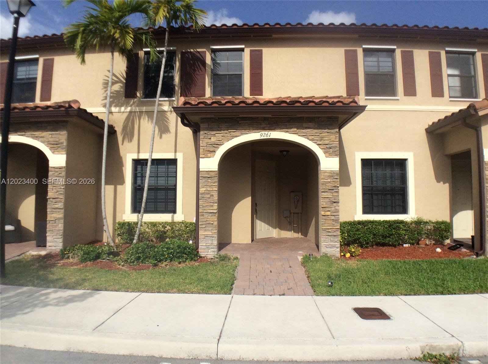 A two-story townhouse exterior features a stone-accented entryway, tan stucco walls, and brown shutters — 9261 W 33rd Way, Hialeah FL 33018, HIALEAH, FL