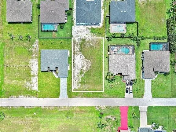 This aerial view shows a vacant residential lot situated between two houses on a street — 1025 NW 35TH PLACE, CAPE CORAL, FL