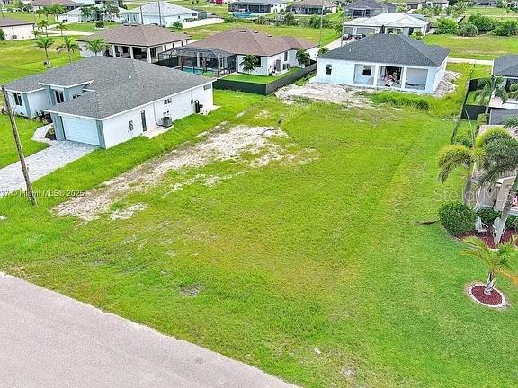 An aerial view shows a vacant grassy lot situated between two modern residential houses — 1025 NW 35TH PLACE, CAPE CORAL, FL