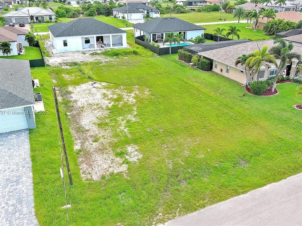 An aerial view shows a vacant residential lot situated between two houses in a neighborhood — 1025 NW 35TH PLACE, CAPE CORAL, FL