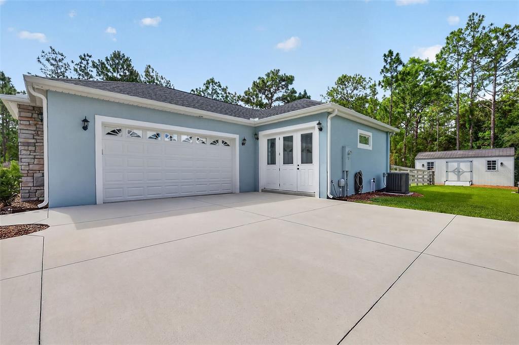 A light blue house exterior features a two-car garage, white double doors, and a shed — 2075 COUNTY ROAD 243F, WILDWOOD, FL