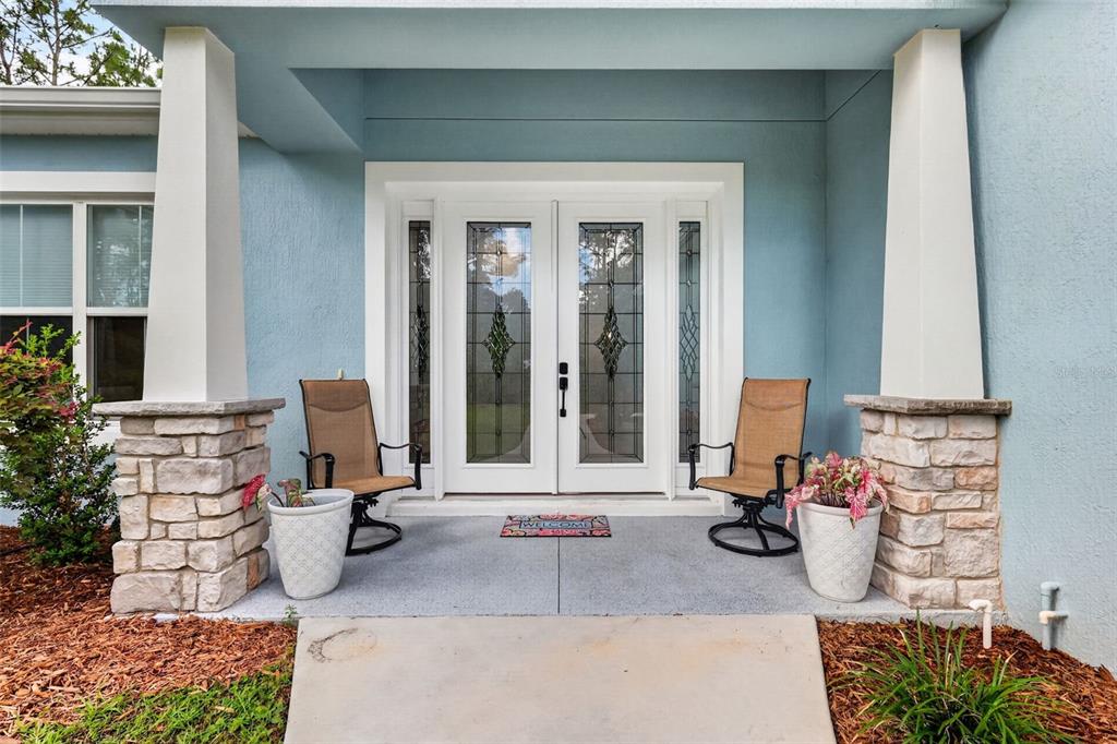 A front porch features two chairs, potted plants, and a double door with glass inserts — 2075 COUNTY ROAD 243F, WILDWOOD, FL