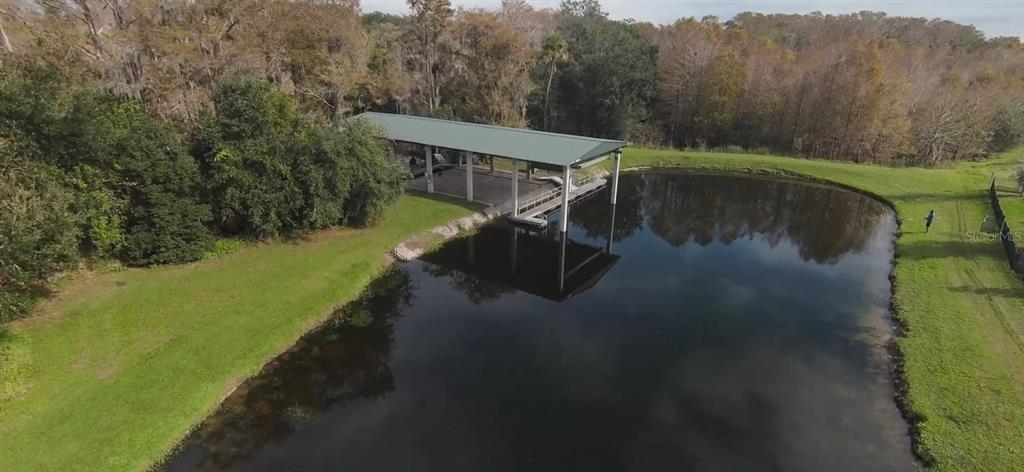 An aerial view shows a covered boat dock situated on a pond near wooded land — 1754 BOAT LAUNCH ROAD, KISSIMMEE, FL
