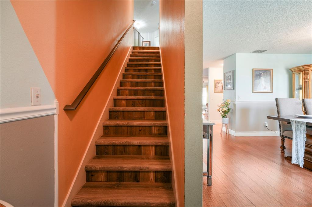 A wooden staircase with an orange wall leads upward next to a dining area — 709 CLIFTON HILLS STREET, ORLANDO, FL