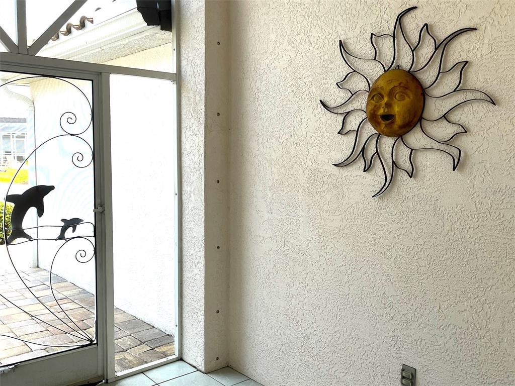 A sun-shaped wall decoration hangs on a textured white wall next to a screened door — 4041 KING TARPON DRIVE, PUNTA GORDA, FL
