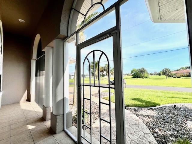 A covered patio with tiled flooring, white columns, and a screen door overlooking a lawn — 24378 BELIZE COURT, PUNTA GORDA, FL