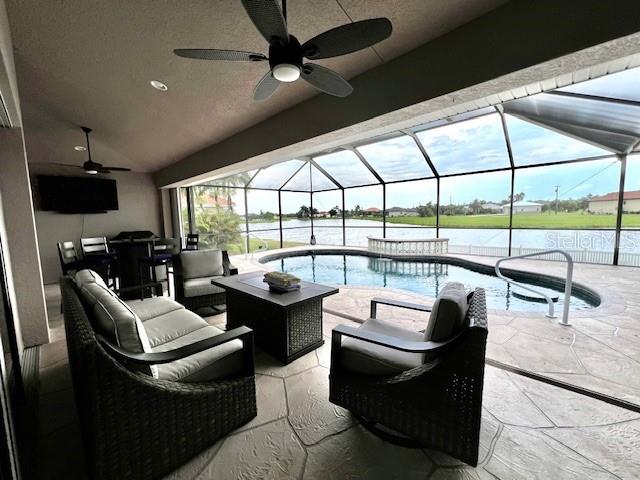 A covered patio features wicker furniture, a ceiling fan, and a pool overlooking a lake — 24378 BELIZE COURT, PUNTA GORDA, FL