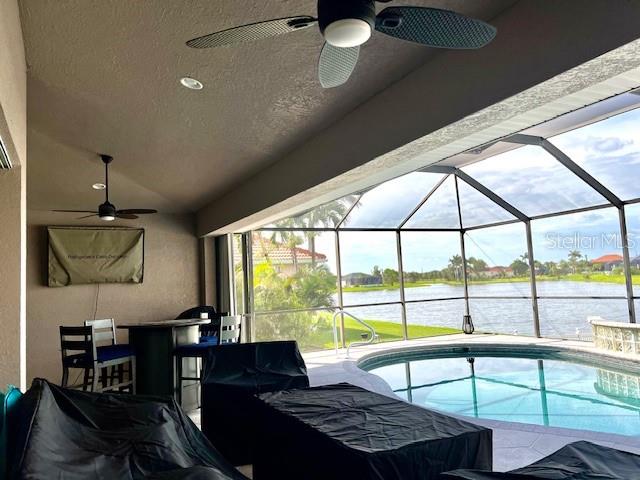 A covered patio features a ceiling fan, outdoor furniture, and a screened-in pool overlooking water — 24378 BELIZE COURT, PUNTA GORDA, FL