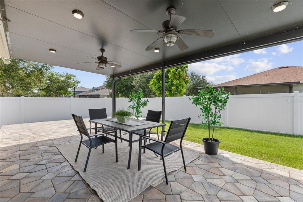 A covered patio features a dining set on a rug, ceiling fans, and a fenced yard — 2719 CYPRESS BOWL ROAD, LUTZ, FL