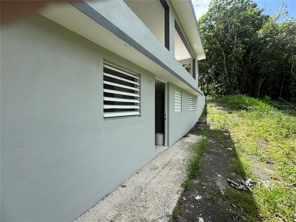 The exterior of a light-colored concrete building features louvered windows and a side entrance door — 156 BO BAYAMONCITO, AGUAS BUENAS, PR