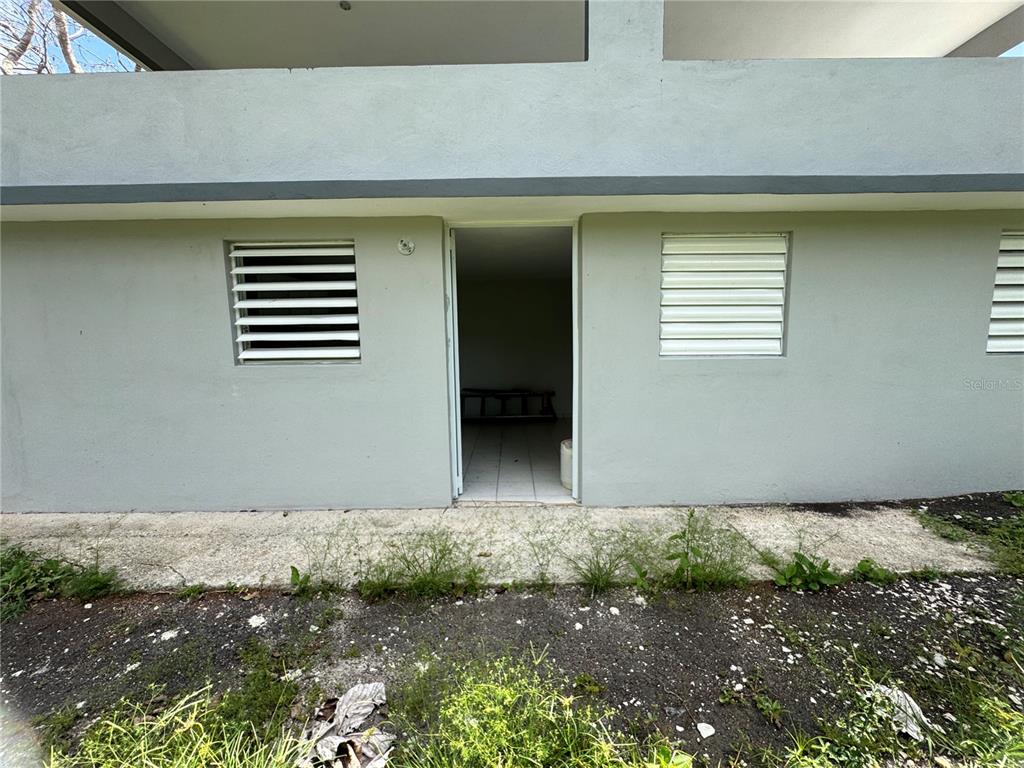 A ground-level exterior view of a building with a central doorway and louvered windows — 156 BO BAYAMONCITO, AGUAS BUENAS, PR