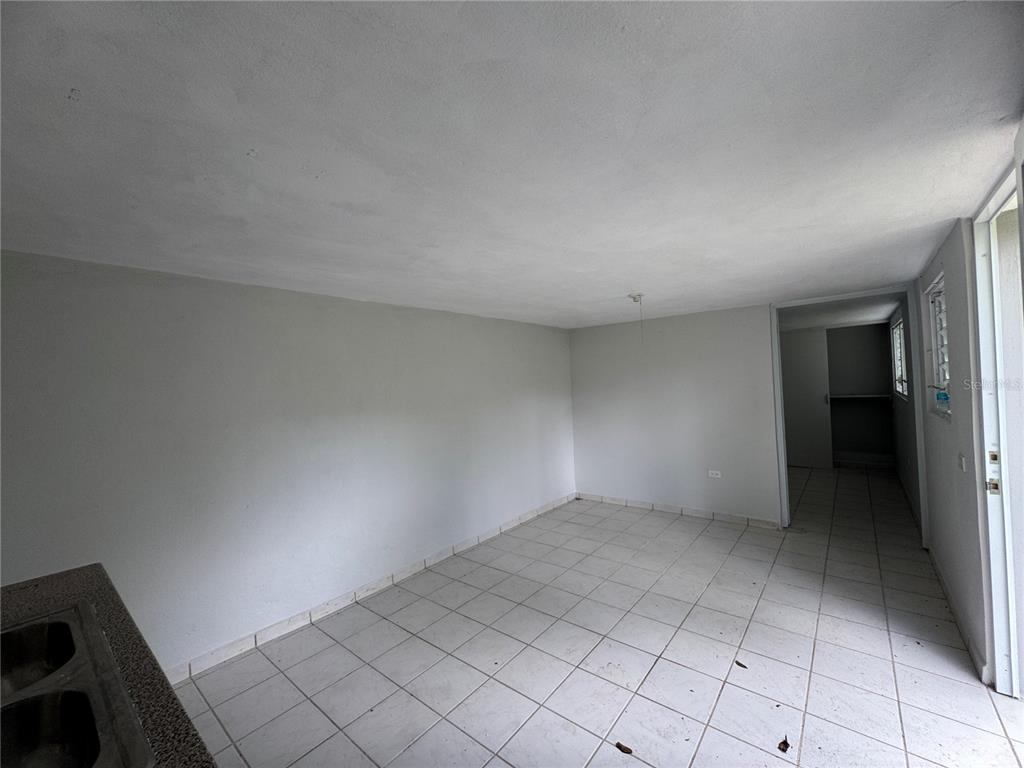 An empty room with white walls, tiled flooring, and a partial view of a kitchen sink — 156 BO BAYAMONCITO, AGUAS BUENAS, PR