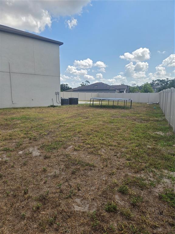 A backyard features a large, empty grass area, a trampoline, and a white vinyl fence — 1876 COLDING DRIVE, RUSKIN, FL