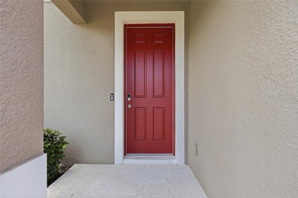 A red front door with a white frame is set into a beige stucco wall — 3924 HANWORTH LOOP, SANFORD, FL