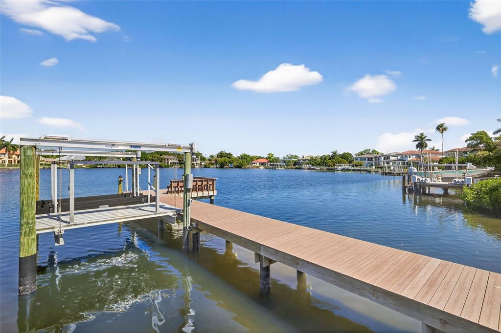 A wooden dock with a boat lift extends into a calm bay under a blue sky — 460 COFFEE POT RIVIERA NE, ST PETERSBURG, FL