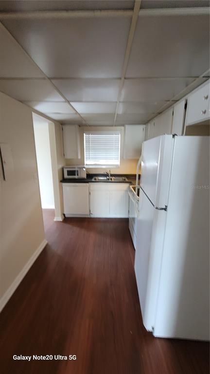 A galley-style kitchen features white cabinets, a white refrigerator, and dark wood-look flooring — 122 N KINGS AVENUE UNIT 202, BRANDON, FL