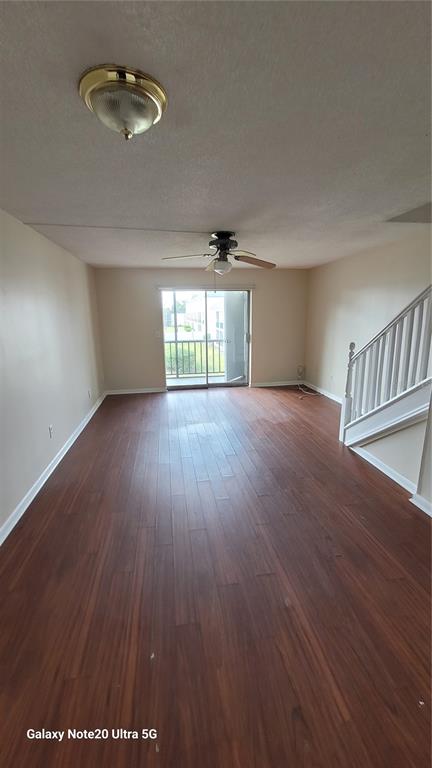 An empty living room features dark wood-look flooring, a ceiling fan, and a sliding glass door — 122 N KINGS AVENUE UNIT 202, BRANDON, FL