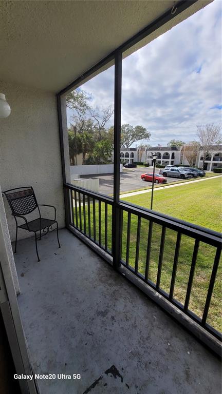 A screened-in balcony features a metal chair overlooking a parking lot and grassy area — 122 N KINGS AVENUE UNIT 202, BRANDON, FL
