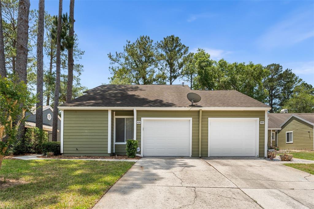 A single-story duplex with olive green siding, two white garage doors, and a concrete driveway — 839 NW 125TH DRIVE, NEWBERRY, FL