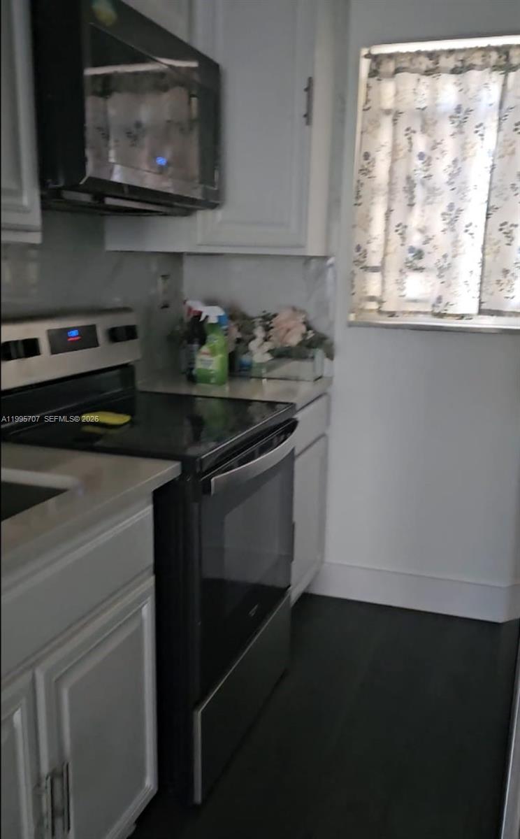 A kitchen features white cabinets, a black stove, a microwave, and a window with curtains — 6055 W 19th Ave # 209, Hialeah FL 33012, HIALEAH, FL