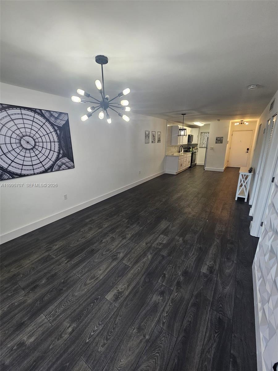 A living area with dark wood-look flooring leads to a kitchen with white cabinetry — 6055 W 19th Ave # 209, Hialeah FL 33012, HIALEAH, FL