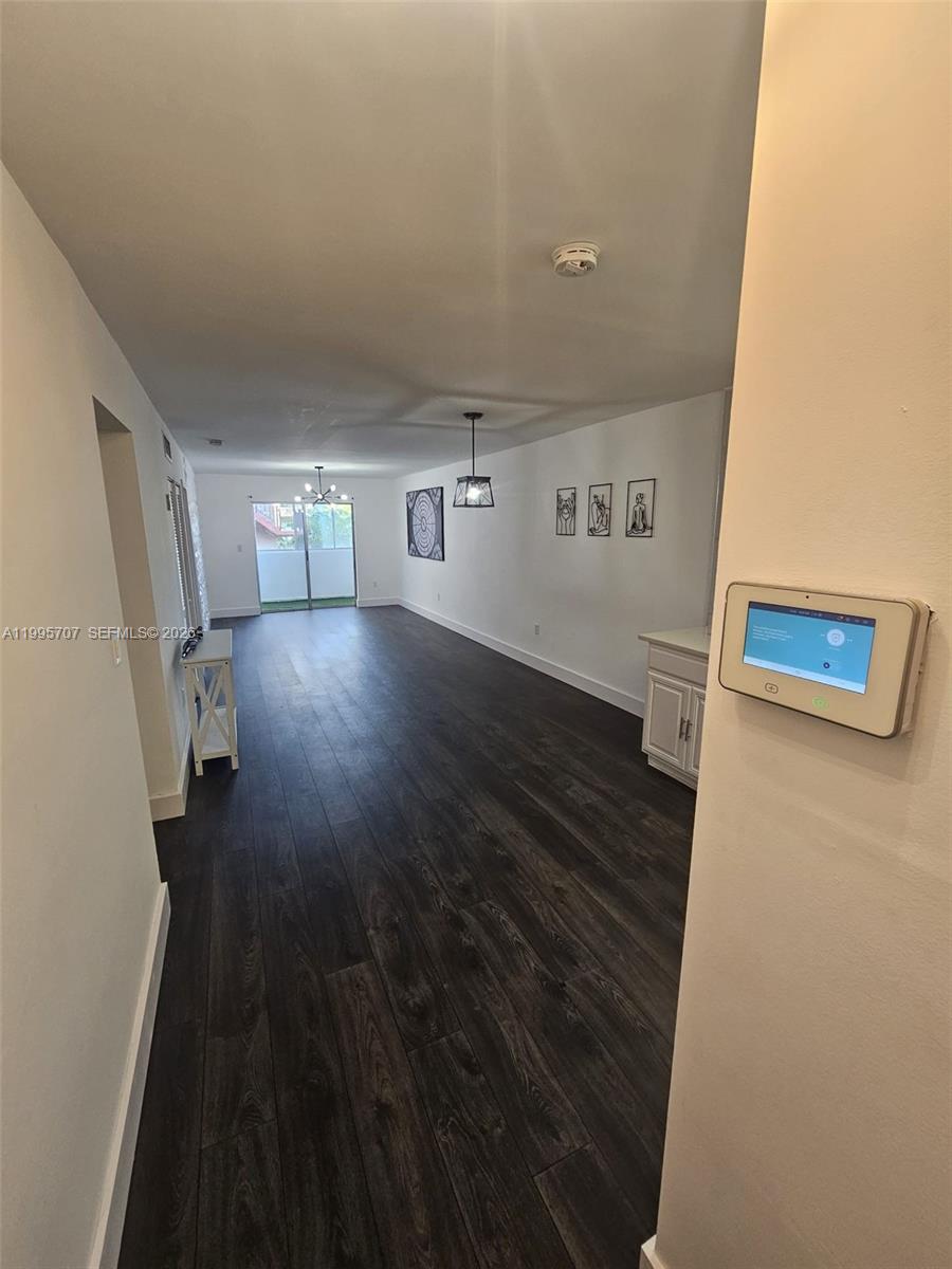 A long, narrow living area features dark wood-look flooring and a wall-mounted smart thermostat — 6055 W 19th Ave # 209, Hialeah FL 33012, HIALEAH, FL