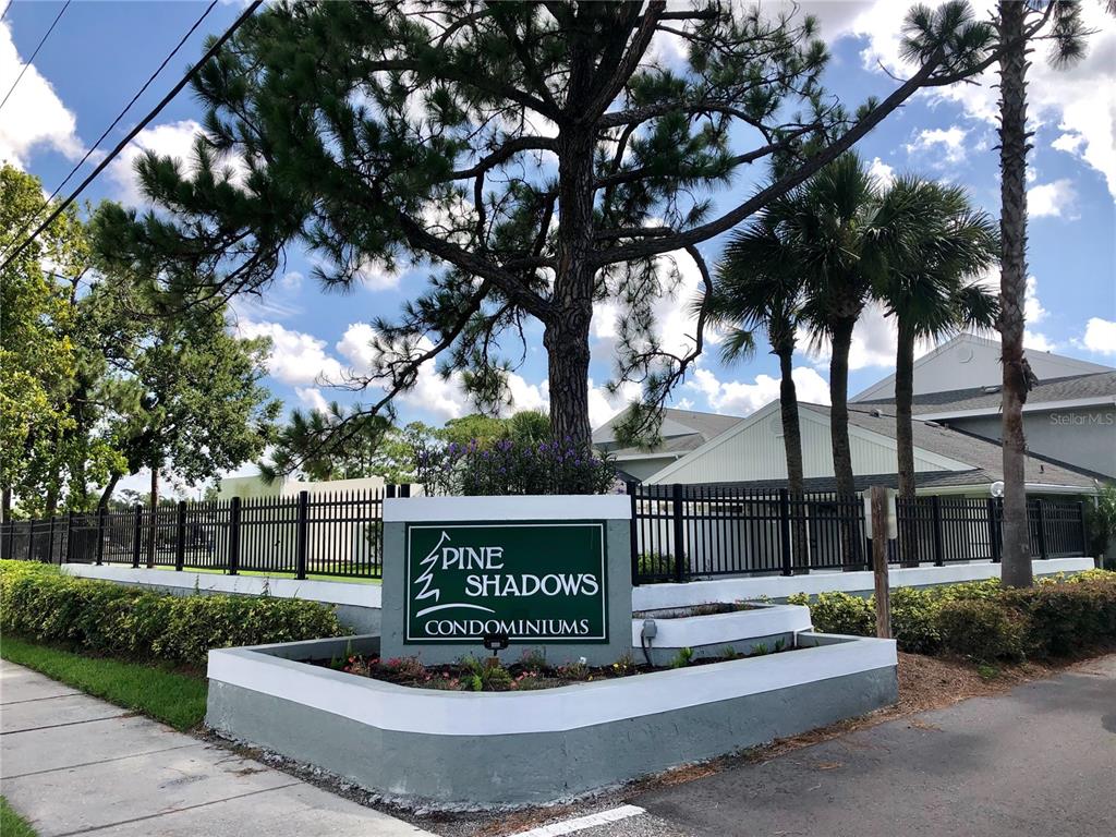 A sign for Pine Shadows Condominiums stands in front of a building and trees — 5613 BLUE SHADOWS COURT UNIT 60-2, ORLANDO, FL