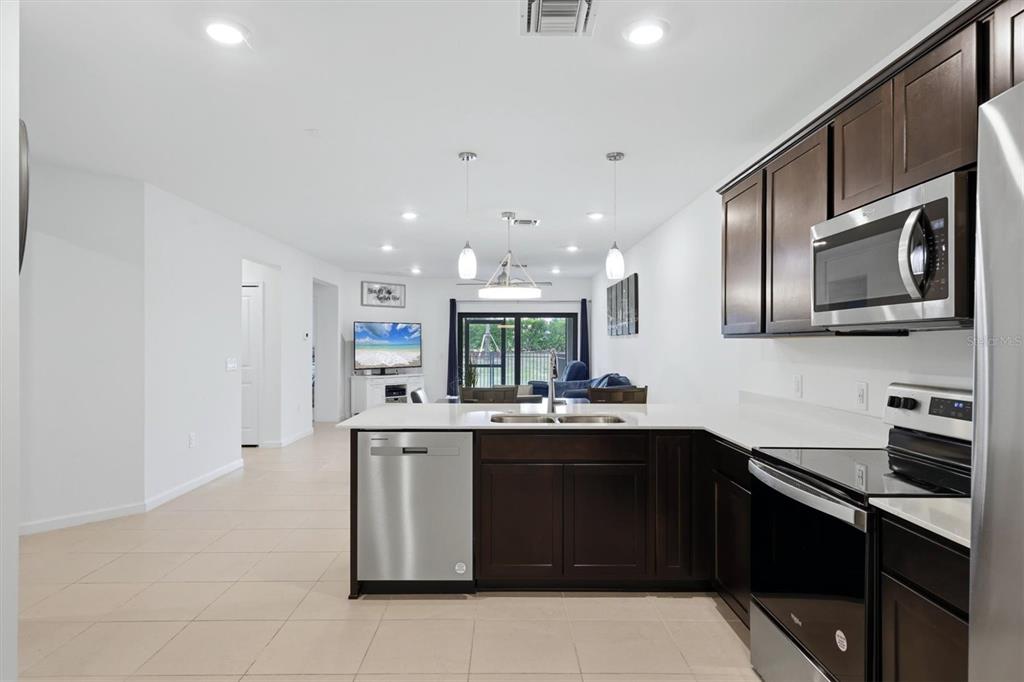 A kitchen with dark wood cabinets and stainless steel appliances opens into a living area — 6499 SILVERSTAR DRIVE, SARASOTA, FL