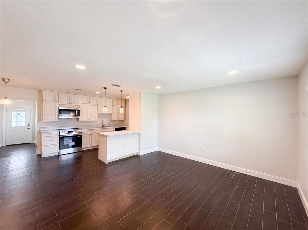 An open-concept kitchen and living area features white cabinetry, stainless steel appliances, and dark flooring — 4147 WILLOW SOUTH DRIVE, MULBERRY, FL