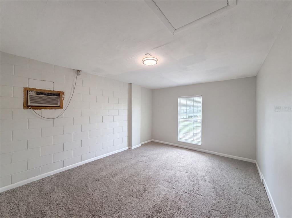 An empty bedroom features gray carpet, light-colored walls, a window, and a wall-mounted air conditioner — 4147 WILLOW SOUTH DRIVE, MULBERRY, FL