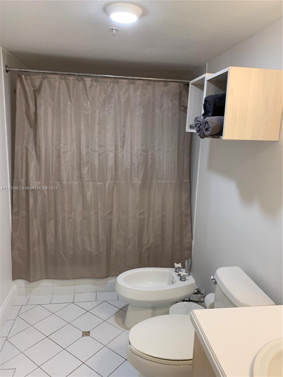 A bathroom features a shower with a tan curtain, a bidet, a toilet, and wall-mounted shelving — 2951 S Bayshore Dr # 417, Miami FL 33133, MIAMI, FL