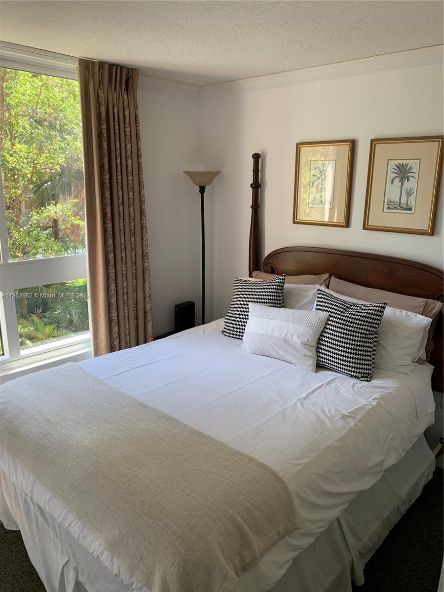 A bedroom features a wooden bed frame, patterned accent pillows, and a window with curtains — 2951 S Bayshore Dr # 417, Miami FL 33133, MIAMI, FL