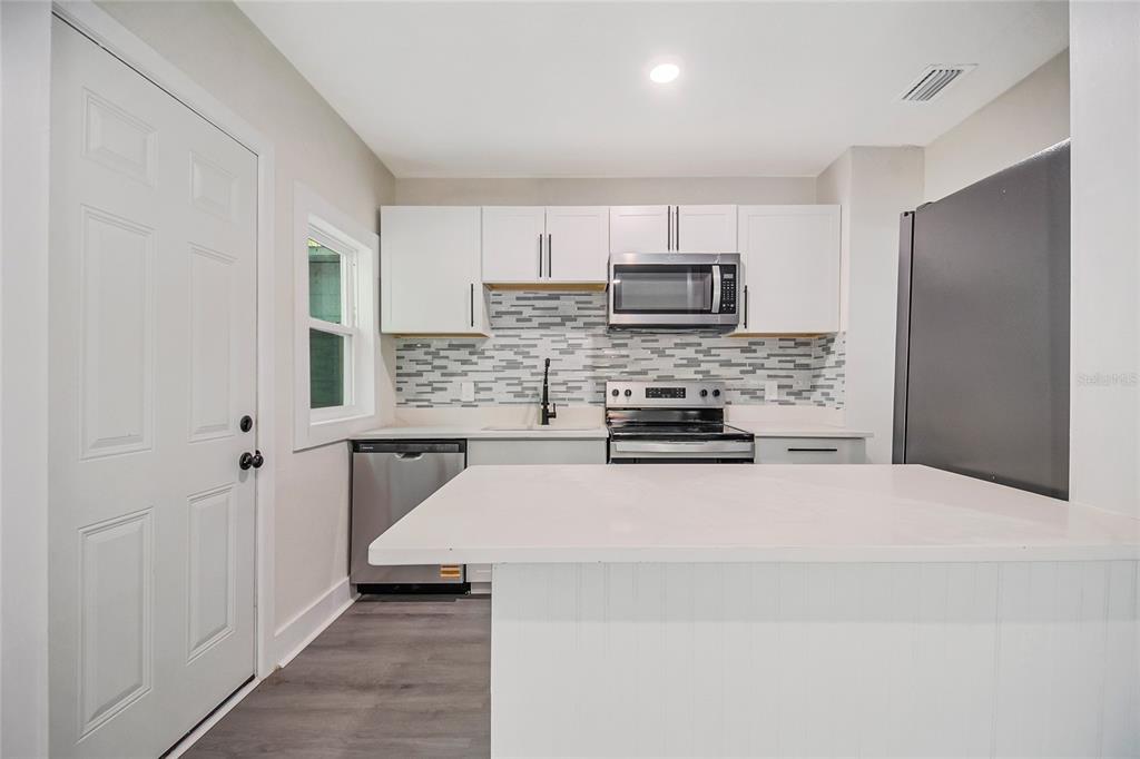 A kitchen features white cabinets, stainless steel appliances, a tiled backsplash, and a white island — 1504 W LINE STREET, LEESBURG, FL