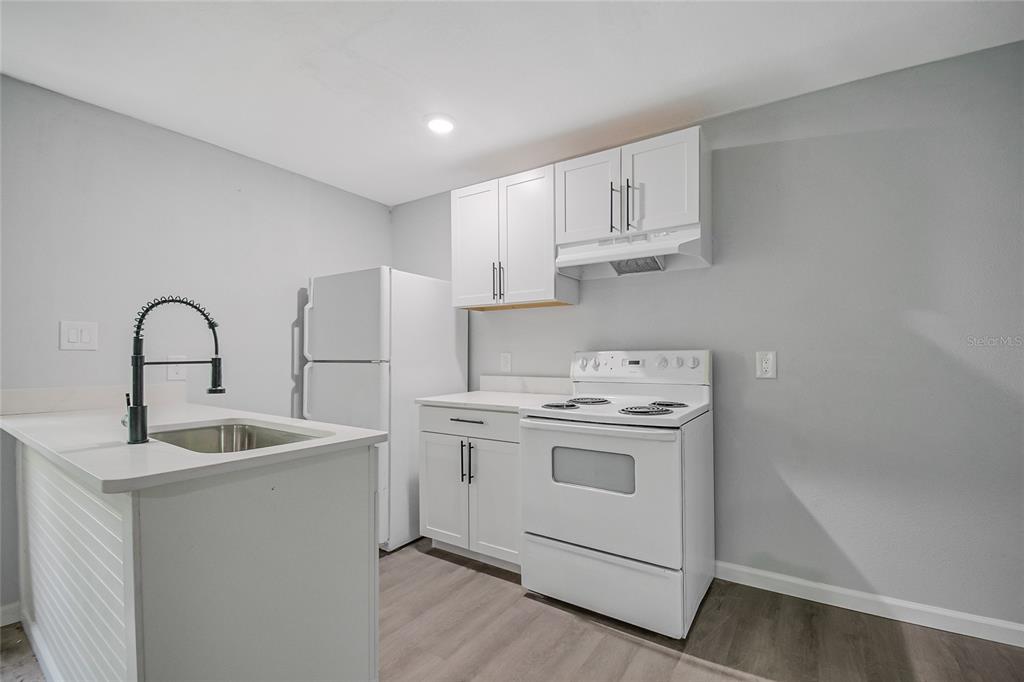 A small kitchen features white cabinets, white appliances, a stainless steel sink, and light flooring — 1504 W LINE STREET, LEESBURG, FL