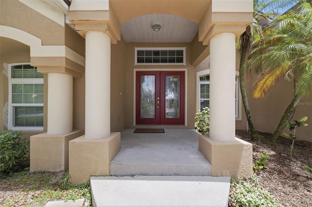 A covered entryway features two large columns, a concrete porch, and red double front doors — 2112 HERITAGE CREST DRIVE, VALRICO, FL