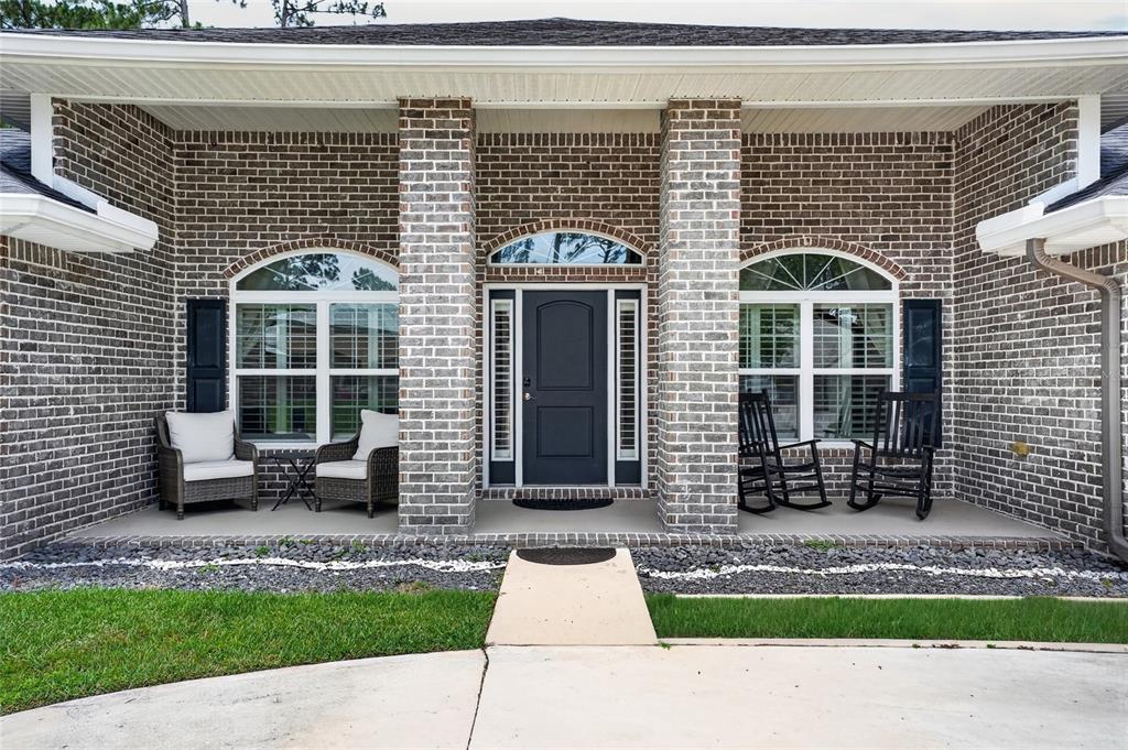 A brick house exterior features a covered front porch with a dark door and rockers — 14 FARNELL LANE, PALM COAST, FL