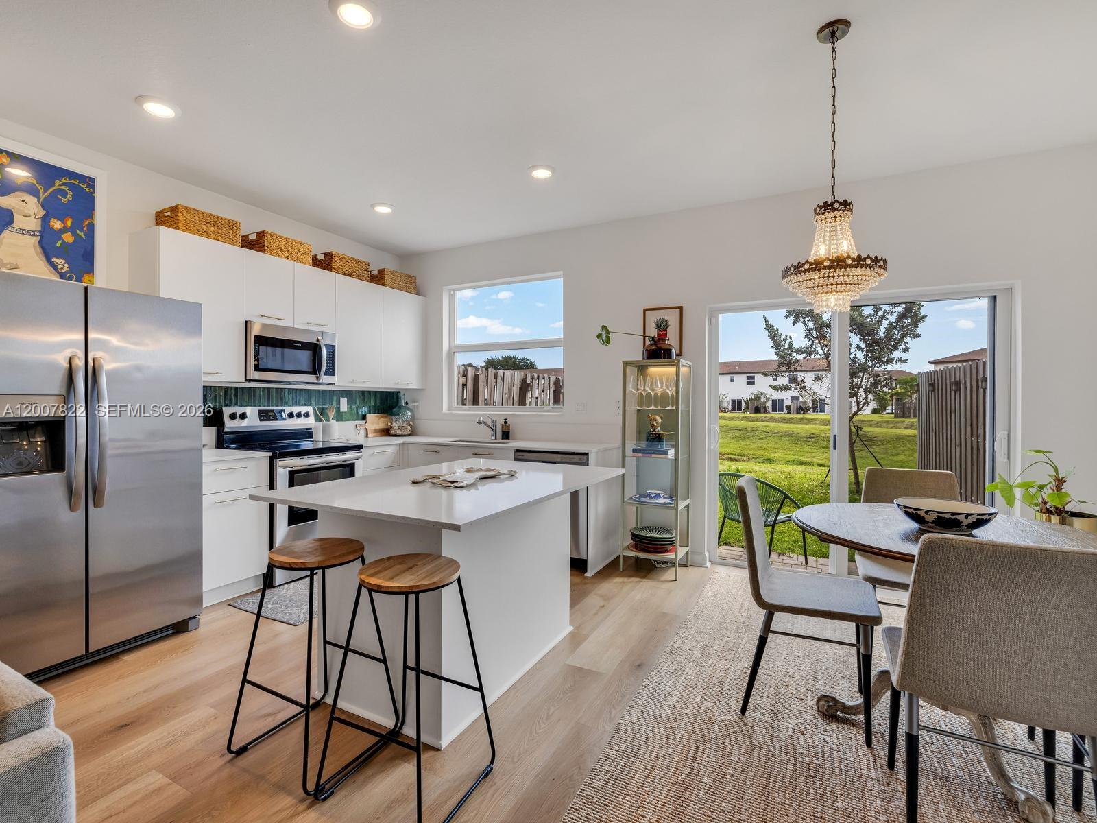 A modern kitchen features white cabinetry, a central island with bar stools, and dining area — 2349 NW 122nd Ter, Miami FL 33167, MIAMI, FL
