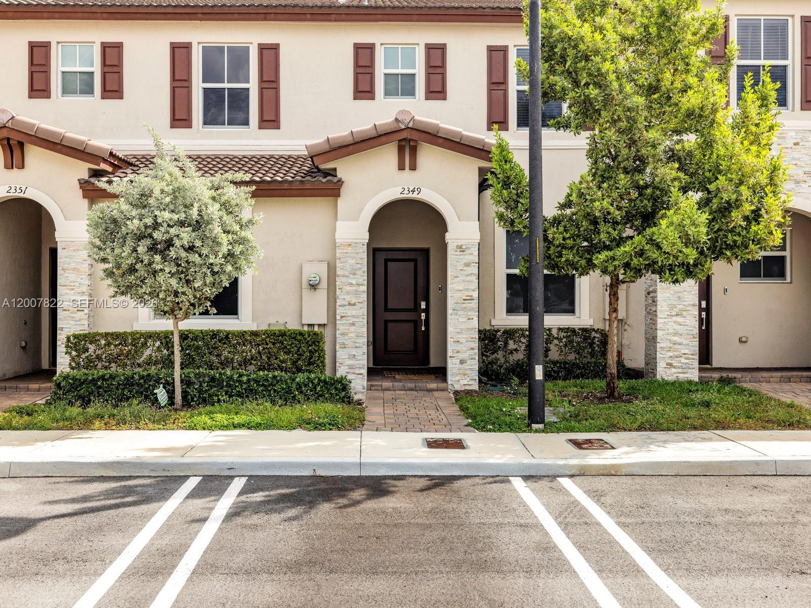A two-story townhouse exterior features a brown front door, stone columns, and a paved walkway — 2349 NW 122nd Ter, Miami FL 33167, MIAMI, FL