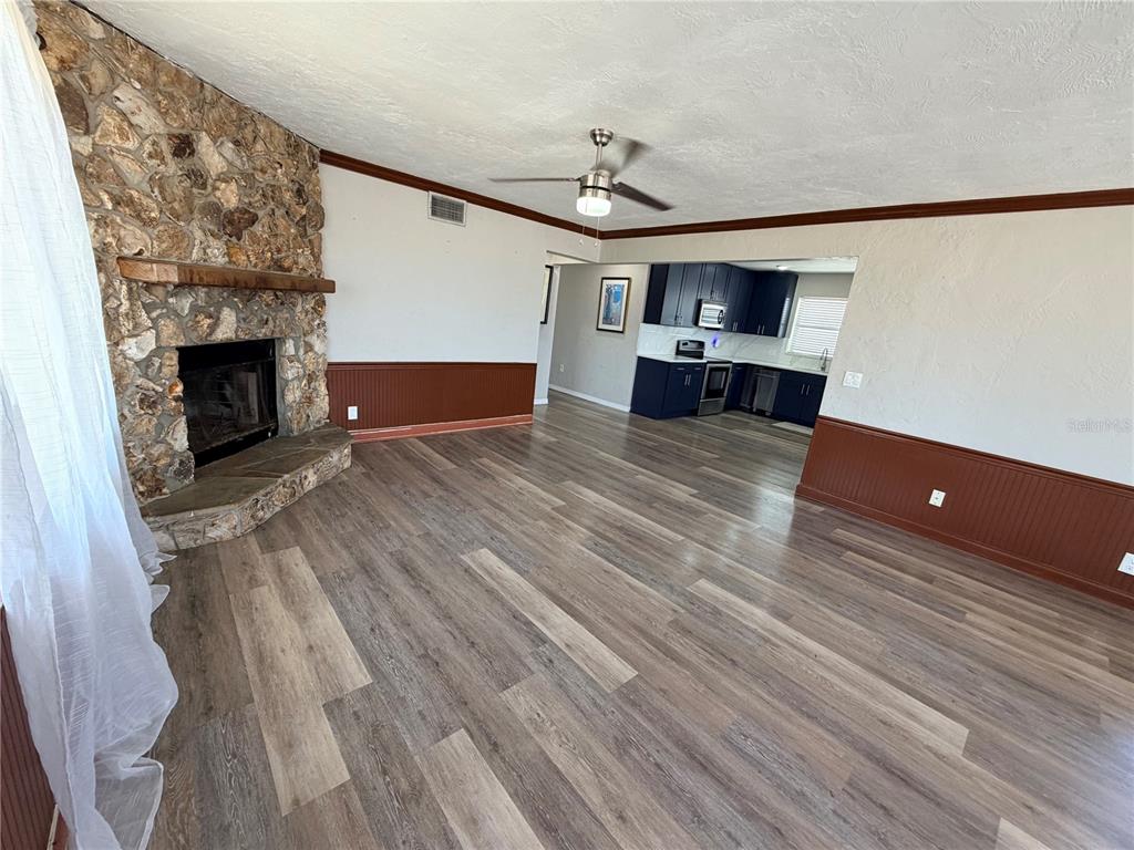 A living room with a stone fireplace, wood-look flooring, and an open kitchen beyond — 538 REVILO BOULEVARD, DAYTONA BEACH, FL