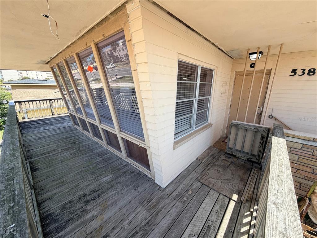 A wooden deck wraps around a building exterior with a screened-in porch and entrance door — 538 REVILO BOULEVARD, DAYTONA BEACH, FL