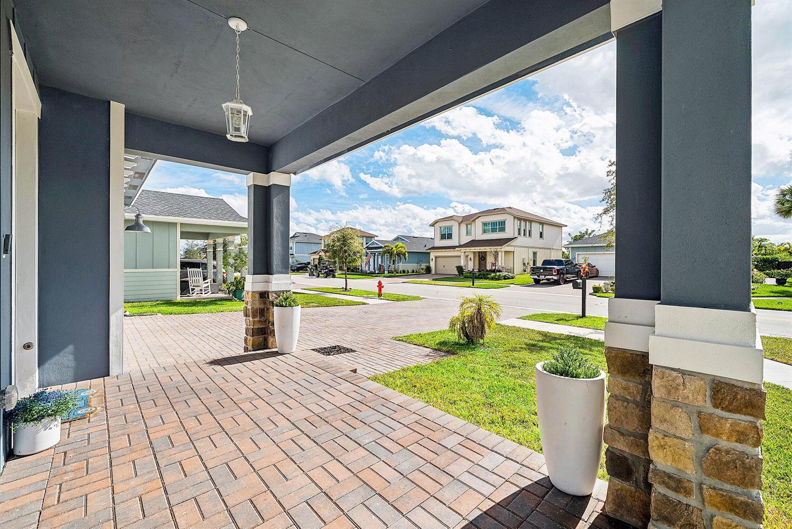 A covered front porch with stone-based columns overlooks a residential street with paved driveways — 19779 Rugged Trunk Trail, FL 33470, FL