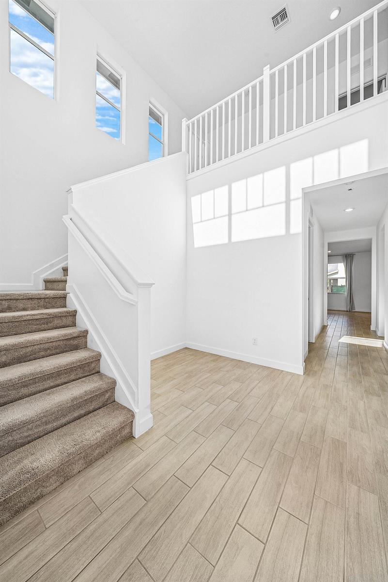 A bright entryway features a carpeted staircase, wood-look tile flooring, and a second-story balcony railing — 19779 Rugged Trunk Trail, FL 33470, FL
