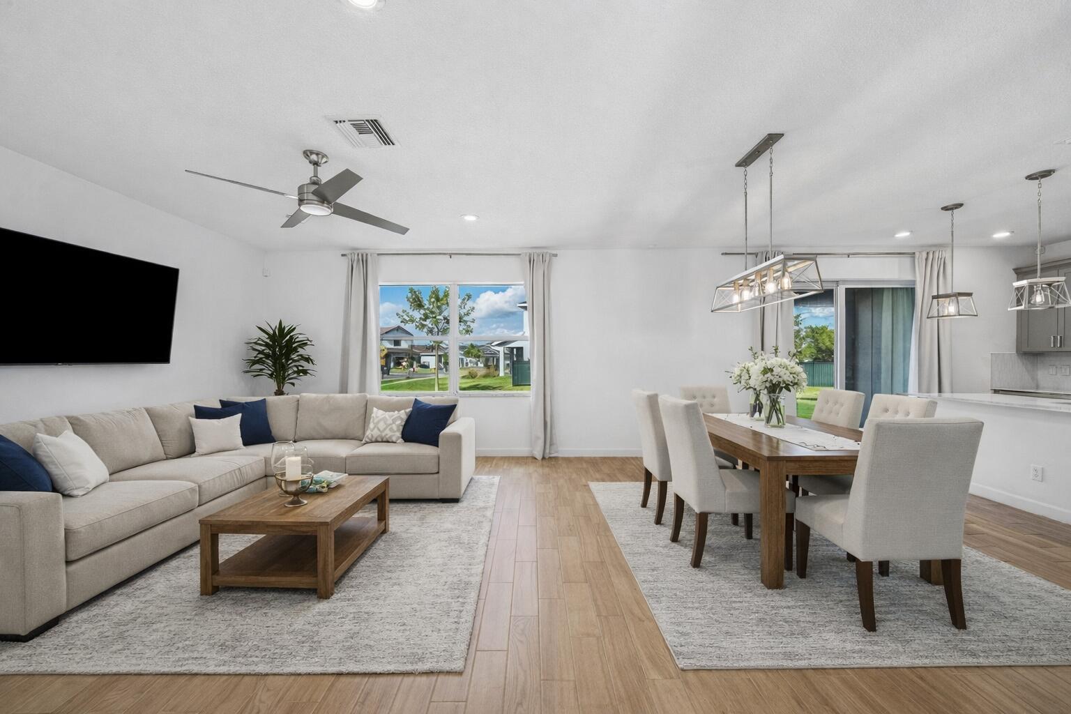 An open-concept living and dining area features light wood-look tile flooring and neutral furniture — 19779 Rugged Trunk Trail, FL 33470, FL