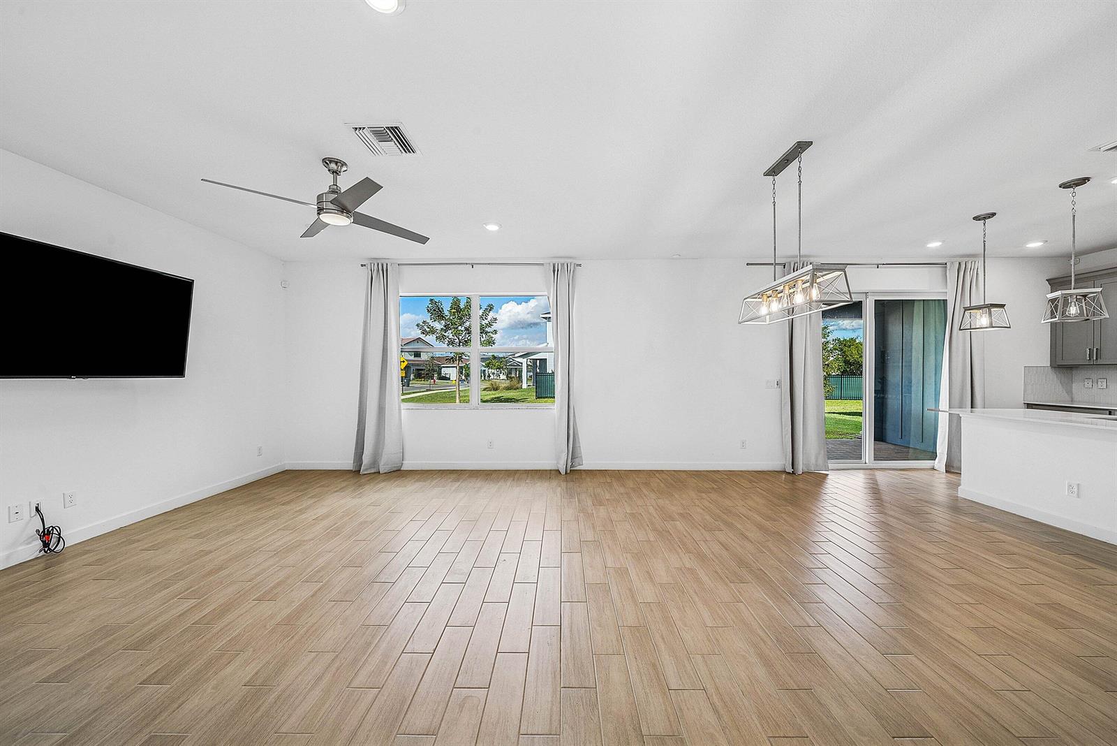 An open-concept living and dining area features light wood-look tile flooring and white walls — 19779 Rugged Trunk Trail, FL 33470, FL