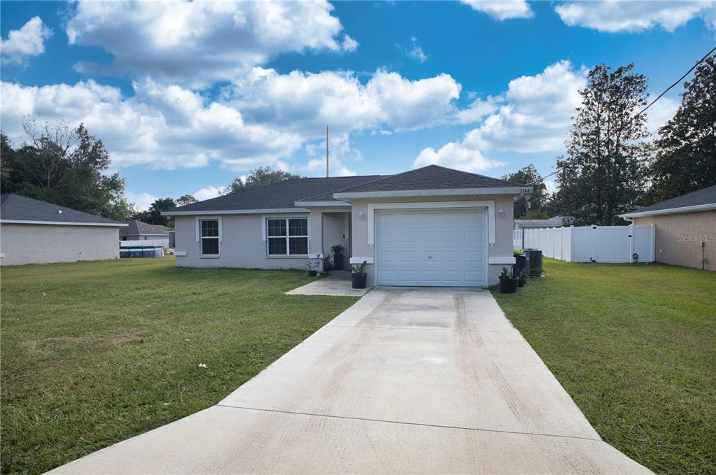 A single-story house with a white garage, beige exterior, and a concrete driveway — 3144 SE 144TH PLACE, SUMMERFIELD, FL