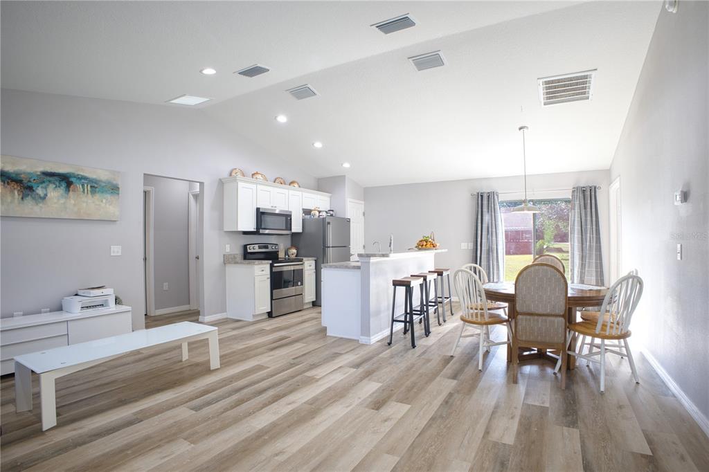 An open-concept kitchen and dining area features white cabinets, stainless appliances, and wood-look flooring — 3144 SE 144TH PLACE, SUMMERFIELD, FL